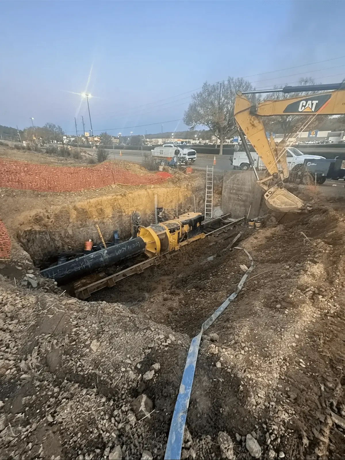 Excavator installing large pipeline in a construction trench.