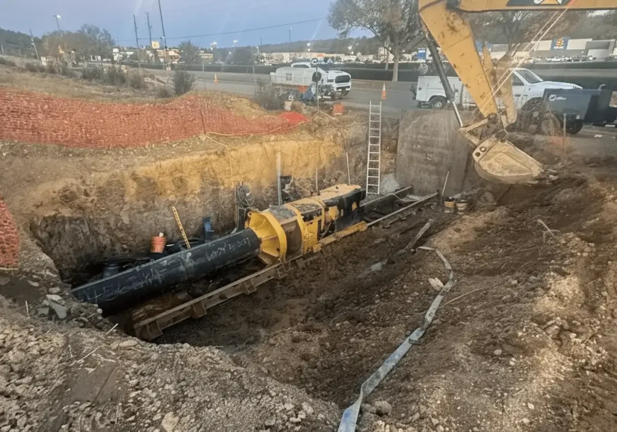Excavator installing large pipeline in a construction trench.