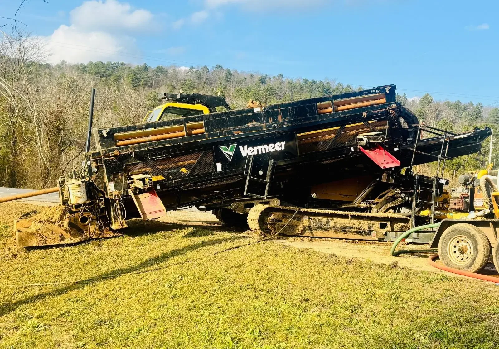 Large black and yellow construction machine on a grassy field near trees.
